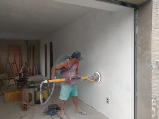 Profissional lixando parede com lixadeira acoplada a aspirador, para controle de poeira